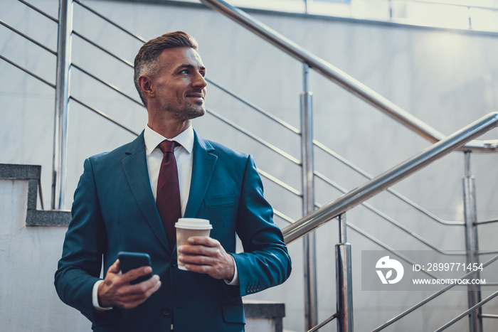 Smiling man with beverage and telephone looking aside