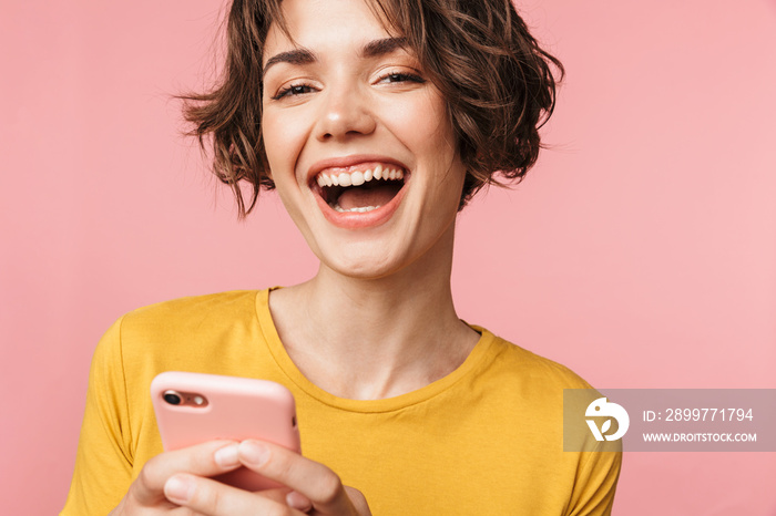 Happy young beautiful woman posing isolated over pink wall background using mobile phone.