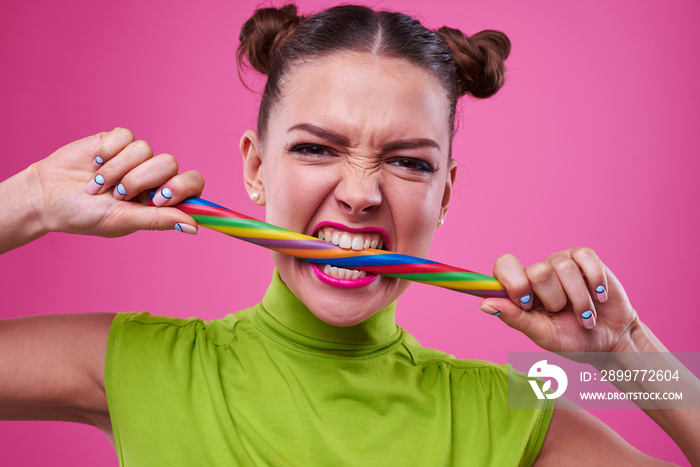 Portrait shot of angry girl biting long lollipop