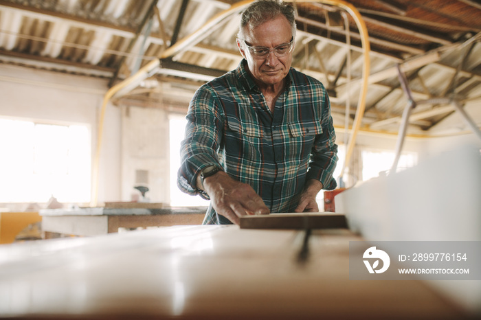 Senior male carpenter working on table saw machine