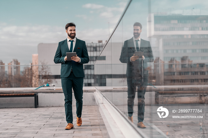 Full length of businessman in formal wear using tablet and walking on the rooftop.