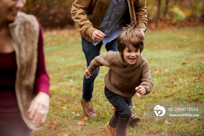 Happy boy running with parents in backyard during autumn