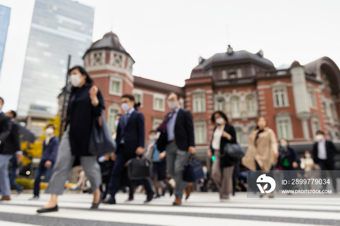 意図的にピントをぼかした東京駅前の横断歩道を渡るマスク姿のビジネスマンたち