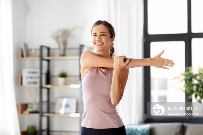 sport, fitness and healthy lifestyle concept - smiling young woman stretching arm at home