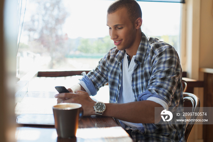 Young adult male texting on phone in coffee shop