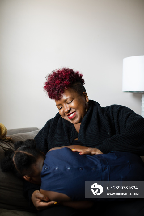 African American mother tickles daughter on couch