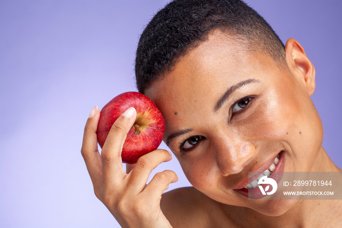 Studio portrait of smiling woman holding apple against purple background