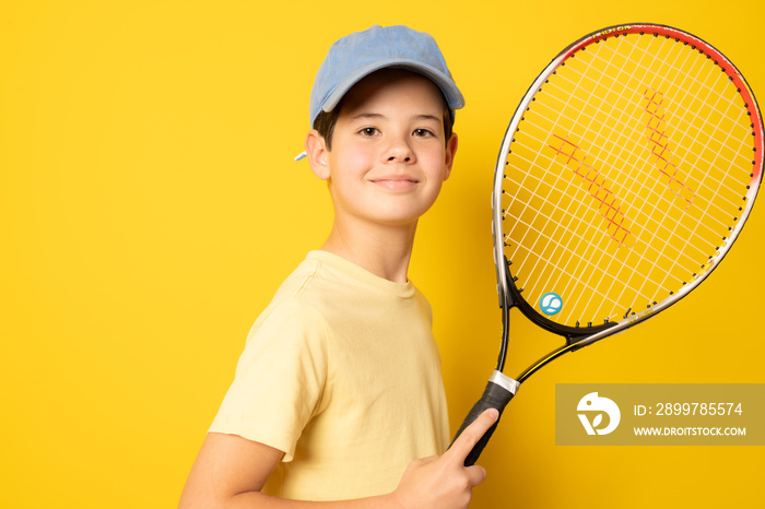 Smiling boy playing tennis holding racket isolated on yellow background