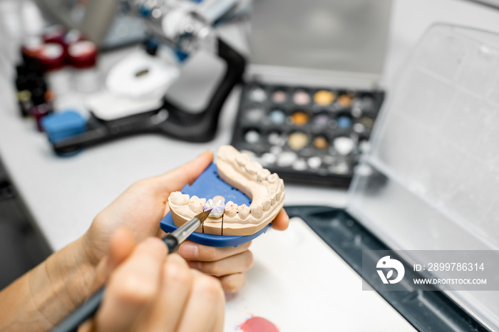 Dental technician coloring dental prosthesis with a paint brush at the laboratory, close-up view. Co