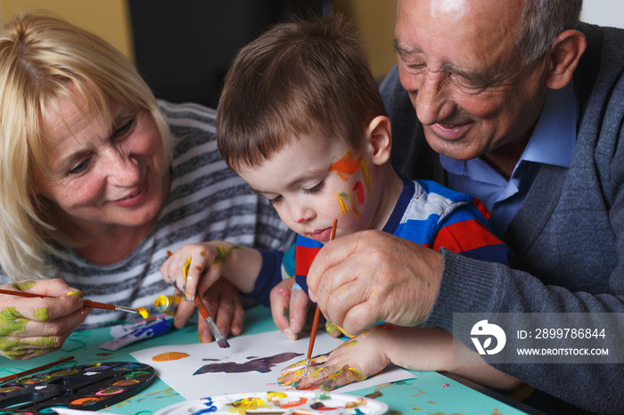 Grandmother and grandfather with grandson drawing together at home.