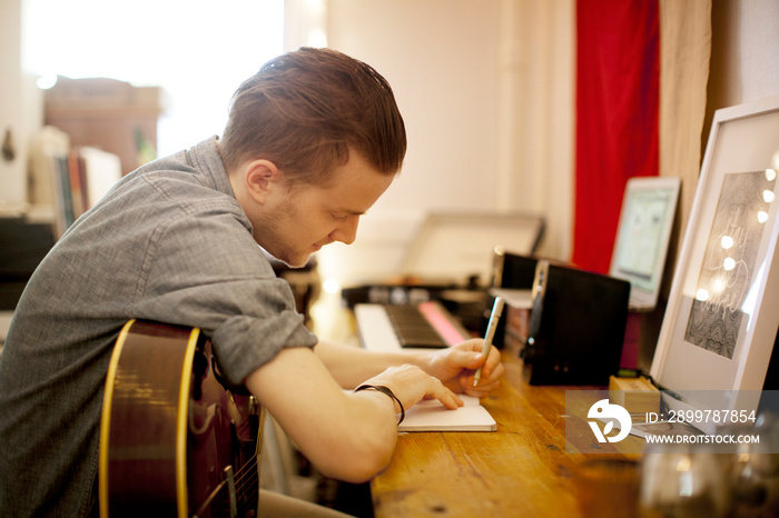一个拿着吉他在桌子上的记事本上写字的男人