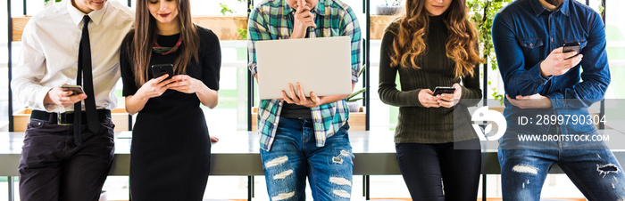 Cropped photo of Group of friends standing on table and everyone use his divices in modern office ro