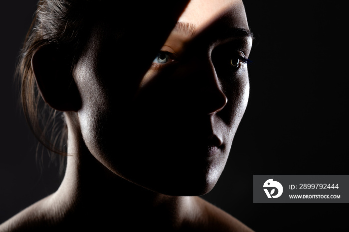 studio portrait of a beautiful young woman with shadows on her face, against dark backgroung,