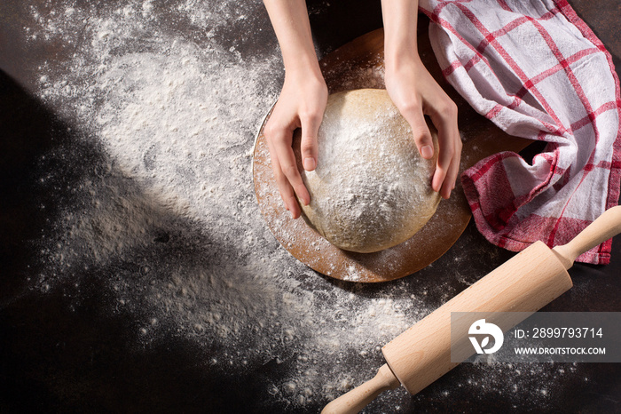 Homemade wholemeal dough for bread and female hands on wooden table with flour, rolling-pin, dark ru