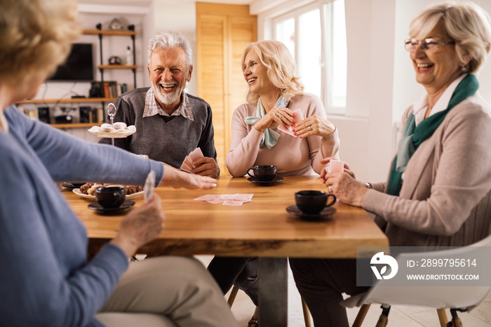 Cheerful senior friends playing cards while gathering at home.