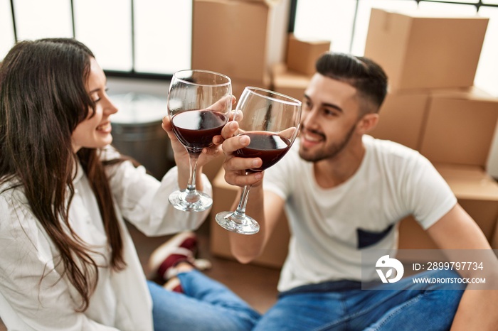 Young hispanic couple smiling happy toasting with red wine at new home.