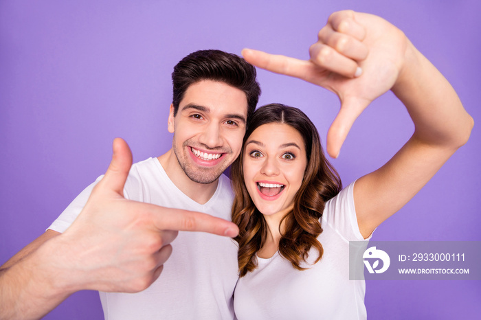 Portrait of positive cheerful spouses students make finger frame imagine they travel trip photographing wear white t-shirt isolated over violet color background