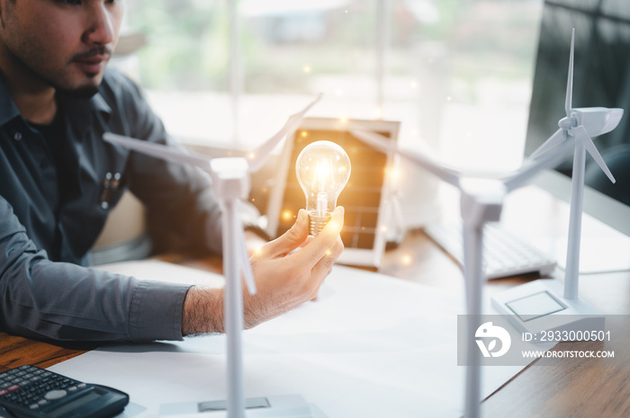 Energy engineer holding light bulb in modern office with solar cell sample and wind turbine model, Creative thinking innovative alternative energy design. Saving nature or ecology concept.