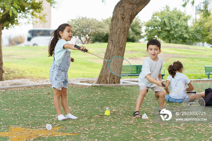 Children playing badminton in park. Young pretty girl and boy playing badminton on summer day. They are about to serve the birdie over the net and so they have a look of concentration on their face.