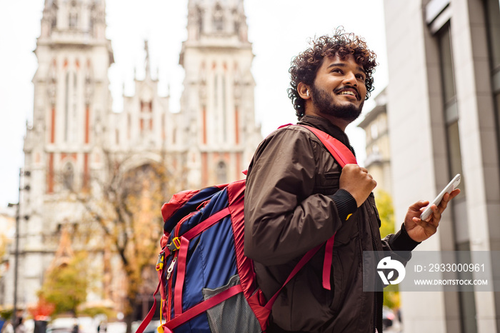 Positive indian traveler with backpack using smartphone in city