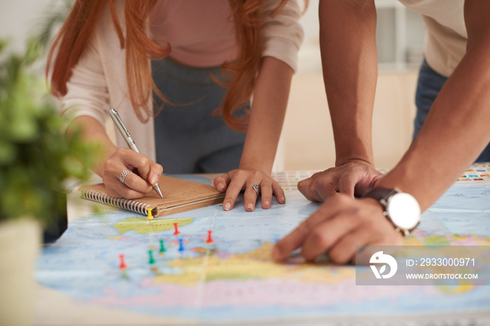 Closeup shot of young couple  marking travelling destinations on map and planning vacation budget