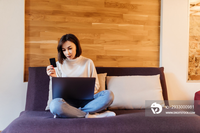 Young woman with laptop shopping on line holding showing credit card