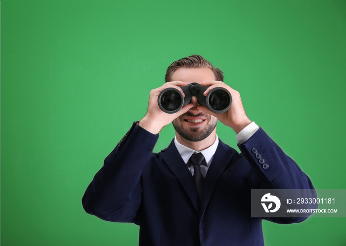 Handsome young man with binocular on color background