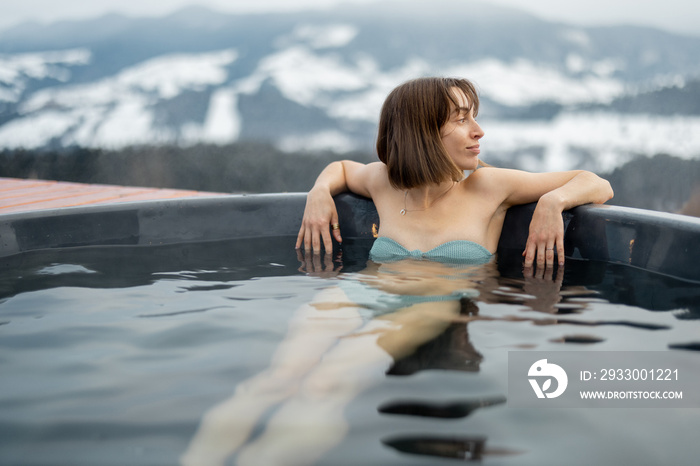 Young woman bathing in hot tub at mountains during winter. Concept of rest and recovery in hot vat on nature. Idea of escape and recreation on mountains