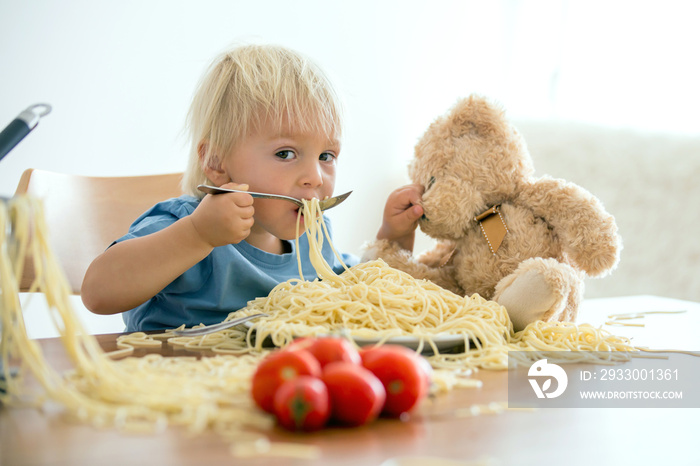 Little baby boy, toddler child, eating spaghetti for lunch and making feeding teddy bear friend