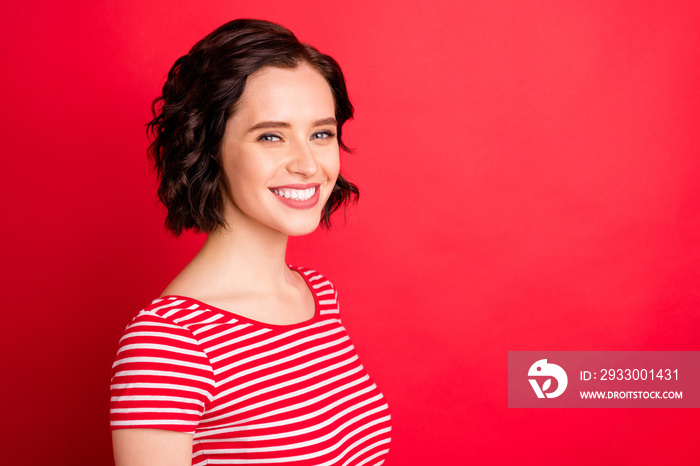 Photo of wonderful wavy curly woman of elation standing in half profile and happily smiling at camera while isolated with red background