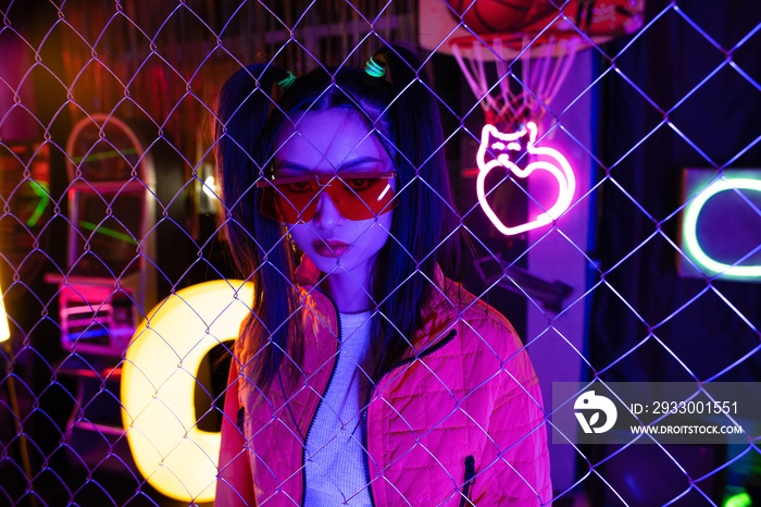 trendy young asian woman in red sunglasses near neon sign and metallic fence