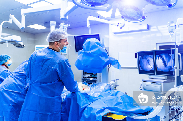 Spinal surgery. Group of surgeons in operating room with surgery equipment. Doctor looking at screen. Modern medical background