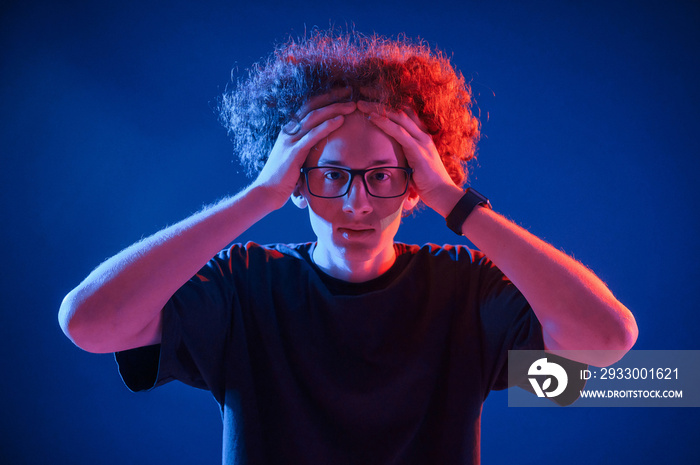 Young man with curly hair is indoors illuminated by neon lighting