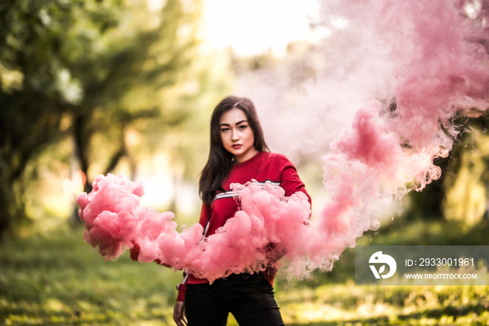 Young asian woman holding red colorful smoke bomb on the outdoor park. Red smoke spreading in the cerebration festival.