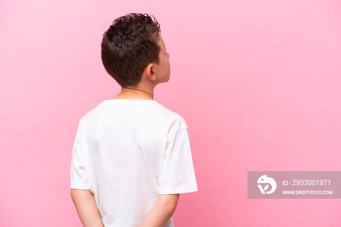 Little caucasian boy isolated on pink background in back position and looking back