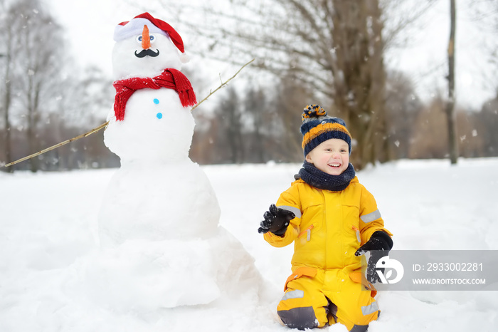 Little boy playing with funny snowman. Active outdoors leisure with children in winter.