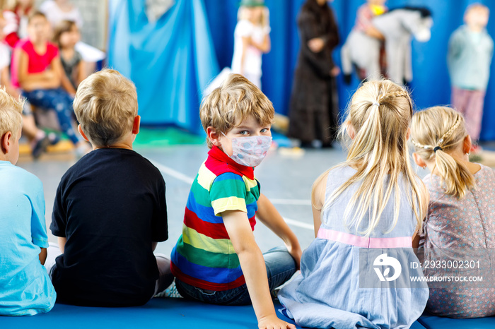 Children watching theater or concert at school. Little kid boy wear medical mask as protection from corona virus on covid quarantine. Kids from back, musical and theatrical performace