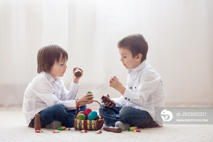 Two adorable little children, boy brothers, having fun eating chocolate bunnies