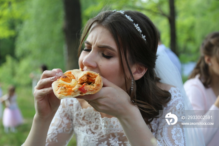 Wedding photo bride eats pizza outdoors in the forest