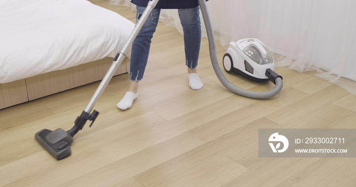 unrecognized woman wife in jeans and apron using vacuum cleaner while cleaning wooden floor at home. housemaid doing housekeeping using machine on wood ground preparing for thanksgiving holiday.