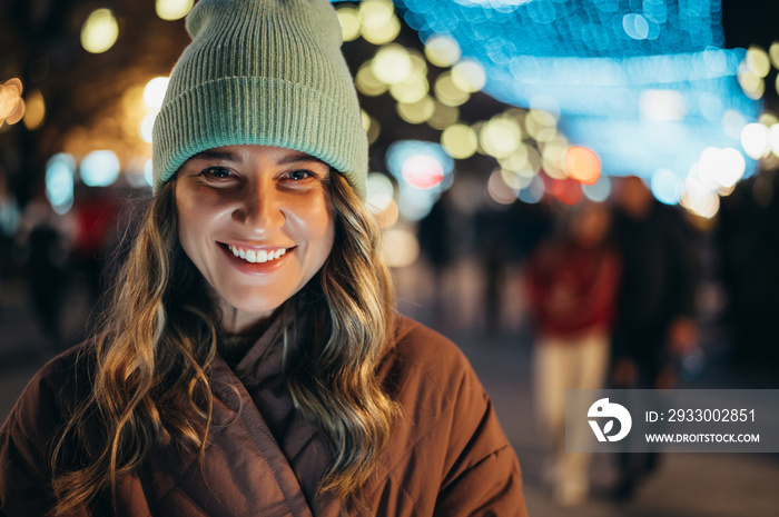 Portrait of a young smiling woman outside with the decorative christmas lights in the background