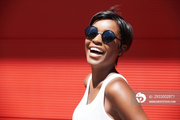 Outdoor portrait of chic African American model in hipster sunglasses posing with happy and cheerful face expression, laughing black female looking excited and carefree, feeling good and enjoying life