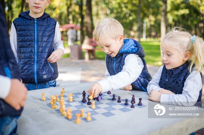 The topic children learning, logical development, mind and math, miscalculation moves advance. large family brothers and sister Caucasian boys and girl playing chess park bright sunny weather autumn