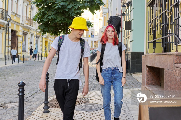 Creative teenagers guy and girl walking and talking along city street