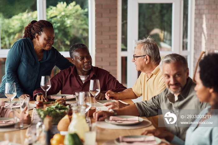 Senior black couple enjoys in lunch with their multiracial family on patio.