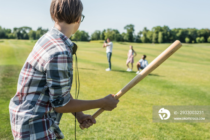 side view of teenage boy holding baseball bat and playing with friends in park