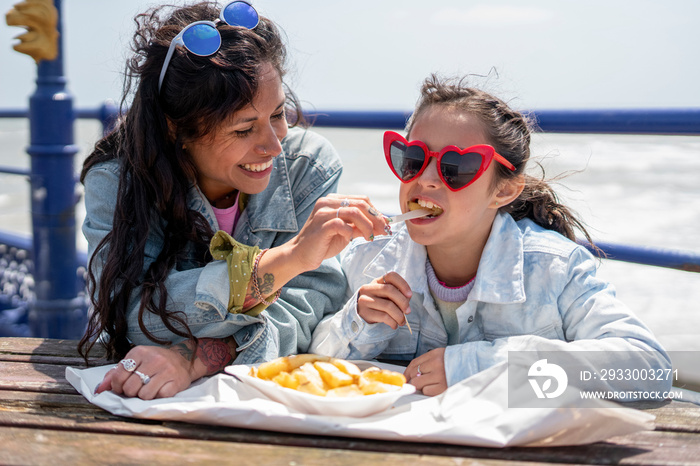 Mother and daughter (8-9) eating fish and chips at seaside