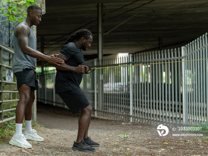 Two men doing strength training with resistance band outdoors