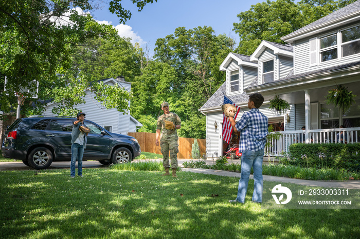 Air Force service member plays catch with sons after coming home from work in uniform.