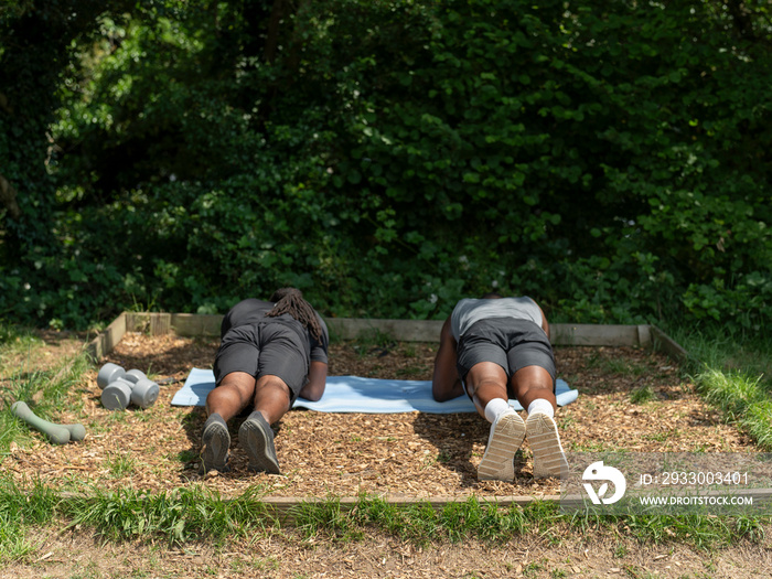 Two men exercising together doing plank in park